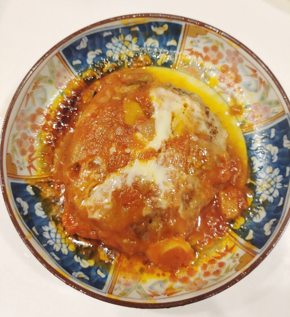 トマトソースと溶けたチーズがかかったハンバーグを和柄の皿に盛った写真 レンジで温めた後