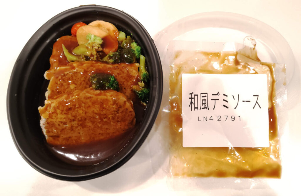 ハンバーグと野菜が入った容器と別添えの和風デミソース